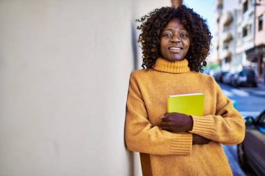 African american woman smiling confident holding book at street