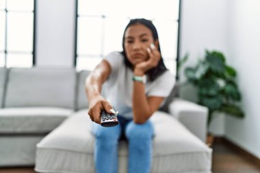 Evde televizyon izleyen genç, sıkıcı Latin kadın.