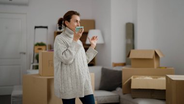 Orta yaşlı İspanyol kadın gülümsüyor. Yeni evindeki akıllı telefondan konuşuyor.