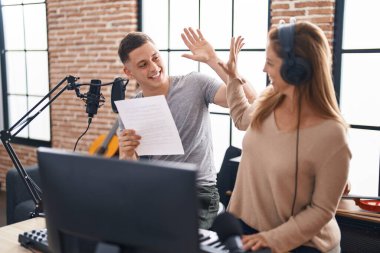 Man and woman musicians singing song high five with hands raised up at music studio