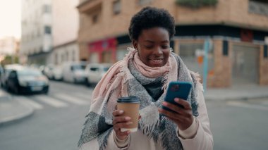 Genç Afrikalı Amerikalı kadın akıllı telefon kullanıyor. Sokakta kahve içiyor.