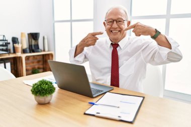 Senior man working at the office using computer laptop smiling cheerful showing and pointing with fingers teeth and mouth. dental health concept. 