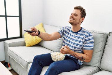Genç İspanyol adam evde film izlerken kendine güvenerek gülümsüyor.