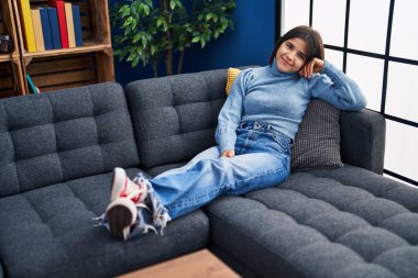 Young beautiful hispanic woman smiling confident lying on sofa at home