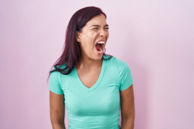 Genç İspanyol kadın pembe arka planda kızgın ve kızgın bağırıyor sinirli ve öfkeli, öfkeyle bağırıyor. öfke ve agresif konsept. 