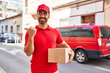 Sakallı, teslimat üniformalı, şapka takan, başparmağını kaldıran ağzı açık gülümseyen genç bir İspanyol. 