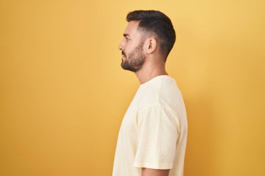 Yakışıklı İspanyol adam sarı arka planda duruyor. Yan tarafa bakıyor, rahat bir görünüm takınıyor ve kendine güvenen bir gülümseme takınıyor.. 