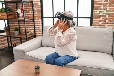 Evde sanal gerçeklik gözlüğü kullanan orta yaşlı bir kadın video oyunu oynuyor.