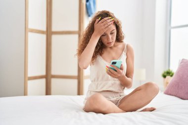 Genç, güzel, İspanyol bir kadın yatak odasında endişeli bir ifadeyle akıllı telefon kullanıyor.