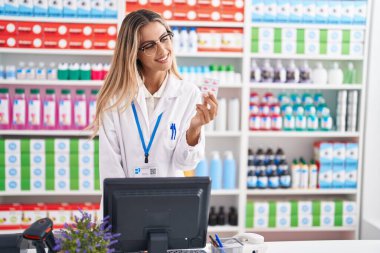 Genç sarışın eczacı eczanede elinde haplarla geziyor.