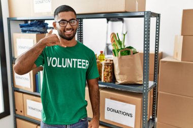 Genç Hintli gönüllü bağış kutusu tutuyor gülümsüyor telefonla el ve parmaklarıyla jest yapıyor telefonda konuşuyor gibi. iletişim kavramları. 