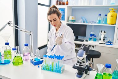 Laboratuvarda çalışan pipet kullanan bilim adamı üniforması giyen genç bir kadın.