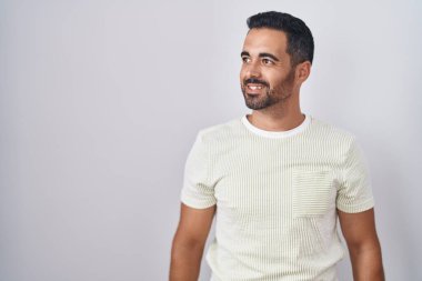 Sakallı İspanyol bir adam soyutlanmış arka planda duruyor. Yüzünde gülümseme, doğal bir ifade ile yan yana bakıyor. Kendinden emin gülen. 