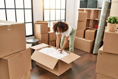 Orta yaşlı İspanyol kadın yeni evinde kutuları açarken gülümsüyor.