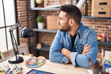 Masada oturan İspanyol genç adam sanat stüdyosunda kollarını kavuşturdu.