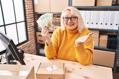 Küçük işletme şirketinde çalışan beyaz bir kadın elinde Hong Kong dolarlarıyla başarıyı mutlu bir gülümsemeyle kutluyor ve kazanan ifade elini kaldırıyor. 