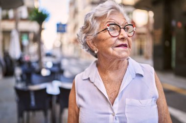 Yaşlı, kır saçlı, gülümseyen bir kadın sokakta kendine güveniyor.