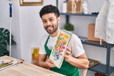 Genç Arap sanatçı gülümsüyor. Sanat stüdyosunda kendine güveni tam.