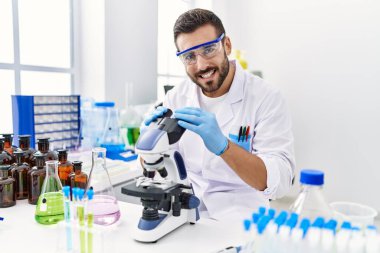 Laboratuvarda mikroskop kullanarak bilim adamı üniforması giyen genç bir İspanyol.