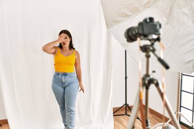 Fotoğrafçılık stüdyosunda model olarak poz veren genç ve güzel bir İspanyol kadın. Şok olmuş bir şekilde yüzünü ve gözlerini kapayarak utanmış bir ifadeyle parmaklarının arasından bakıyor.. 