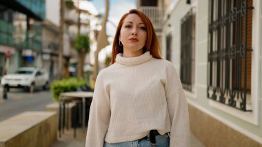 Sokakta ciddi bir ifadeyle duran genç kızıl saçlı kadın.