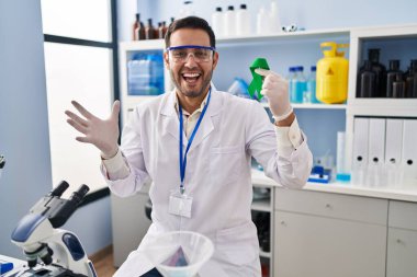 Sakallı genç İspanyol adam elinde yeşil kurdeleyle laboratuvarda çalışıyor zaferi mutlu bir gülümsemeyle kutluyor ve ellerini kaldırarak ifade ediyor. 