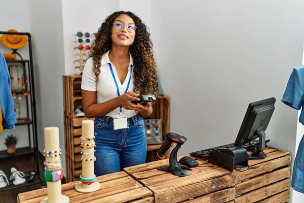 Genç Latin esnaf mağazasında veri telefonu kullanarak mutlu bir şekilde gülümsüyor..