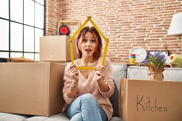 Yeni evindeki kanepede oturan genç beyaz kadın çılgınlığı kutluyor ve başarıya hayret ediyor gözleri açık heyecanla bağırıyor. 