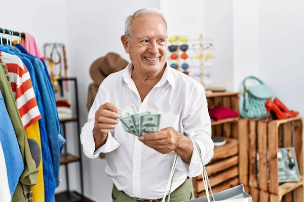 Senior man customer smiling confident counting dollars at clothing store
