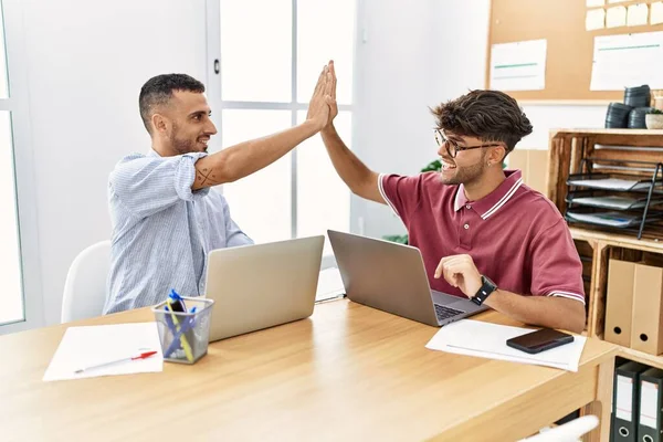 Two business workers smiling happy high five with hands raised up at the office.