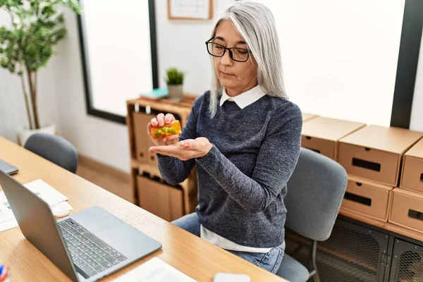 中年白发女商人在办公室工作时吃药 — 图库照片