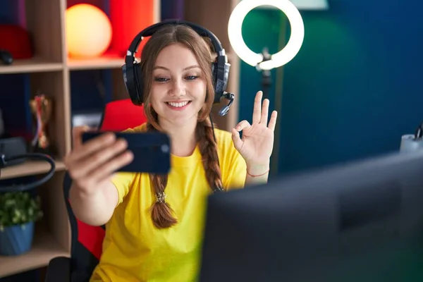年轻的高加索女人用智能手机玩电子游戏 手拿着手签 微笑友善地摆设着极好的象征 — 图库照片