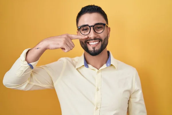 ヒスパニック系の若い男が顔や鼻に手指で指してビジネス服や眼鏡を着て 陽気な笑顔 美の概念 — ストック写真