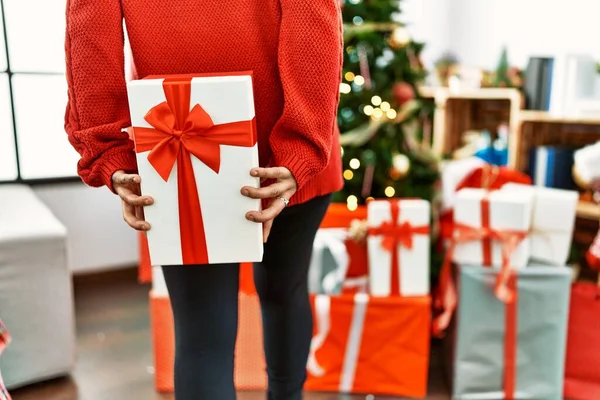Young Hispanic Woman Holding Gift Back Standing Christmas Tree Home — Stock Photo, Image