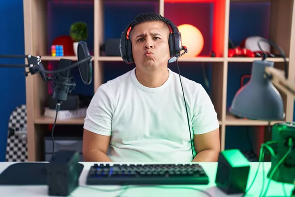 Young hispanic man playing video games looking at the camera blowing a kiss on air being lovely and sexy. love expression.