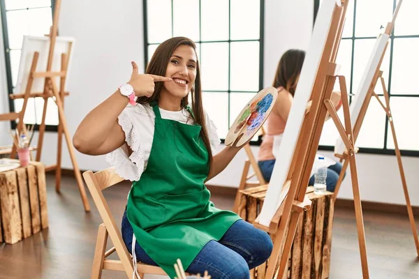 若いヒスパニックアーティストの女性は アートスタジオでキャンバスに絵を描いて 指の歯と口で陽気に見せて指摘して笑っています 歯の健康の概念 — ストック写真