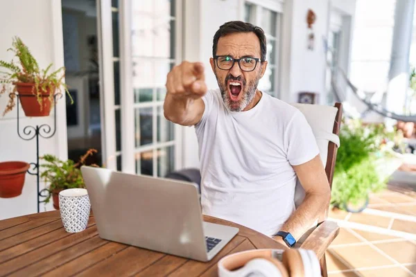 Middle age man using computer laptop at home pointing displeased and frustrated to the camera, angry and furious with you