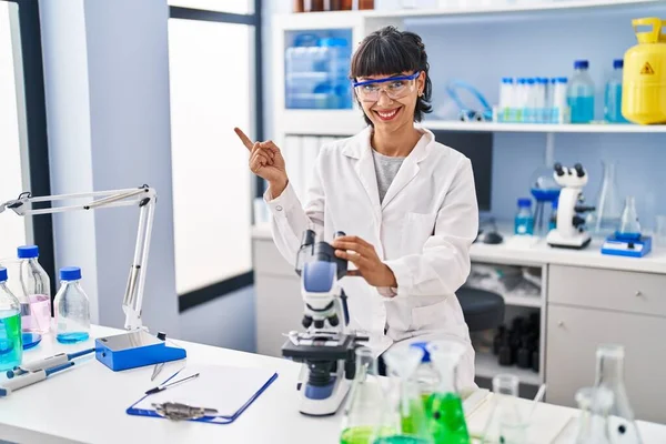 Mladá Hispánka Pracující Laboratoři Vědců Šťastně Usmívá Ukazujíc Rukou Prstem — Stock fotografie