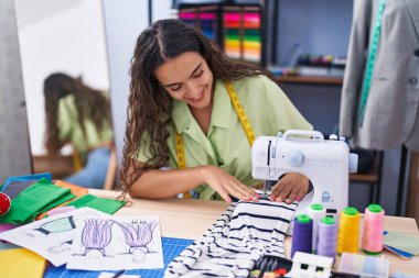 Elbise fabrikasında dikiş makinesi kullandığından emin bir şekilde gülümseyen güzel İspanyol kadın.
