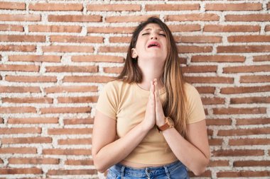 Genç esmer kadın tuğlaların üzerinde duruyor. Elleriyle yalvarıyor ve dua ediyor. Yüzünde umut ifadesi var. Yalvarıyor. 