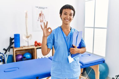 Kısa saçlı, İspanyol bir kadın ağrı kesici kliniğinde çalışıyor gülümsüyor ve el ve parmaklarıyla 