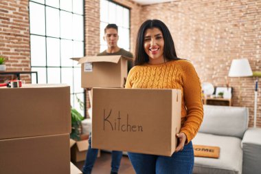 Karton kutularla yeni bir eve taşınan genç çift kameraya seksi bir ifadeyle bakıyor, neşeli ve mutlu bir yüzle.. 