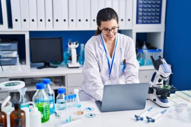 Laboratuvarda çalışan genç İspanyol bilim kadını dizüstü bilgisayar kullanıyor.