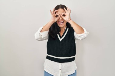 Tecrit edilmiş arka planda duran genç İspanyol kadın dürbün gibi jest yapıyor, gözleri parmaklarından bakıyor. çılgın ifade. 