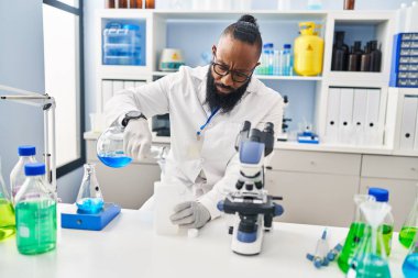 Genç Afrikalı Amerikalı adam bilim adamı üniforması giyiyor. Laboratuvarda sıvı ölçüyor.