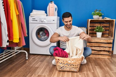 Çamaşır odasında kendine güvenen genç İspanyol adam gülümsüyor.