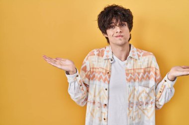 Sıradan bir yaz gömleği giyen, elleri ve kolları havada, kafası karışmış genç bir adam. şüphe kavramı. 