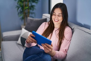 Evdeki koltukta oturan dokunmatik ped kullanan genç bir kadın.