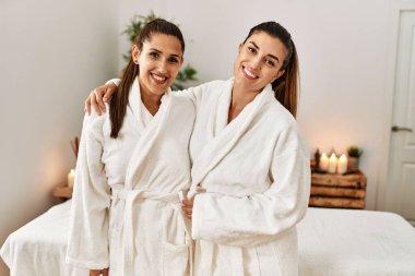 İki kadın bornoz giyiyor. Güzellik merkezinde birbirlerine sarılıyorlar.