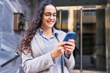 Genç İspanyol kadın yönetici caddede akıllı telefon kullanıyor.